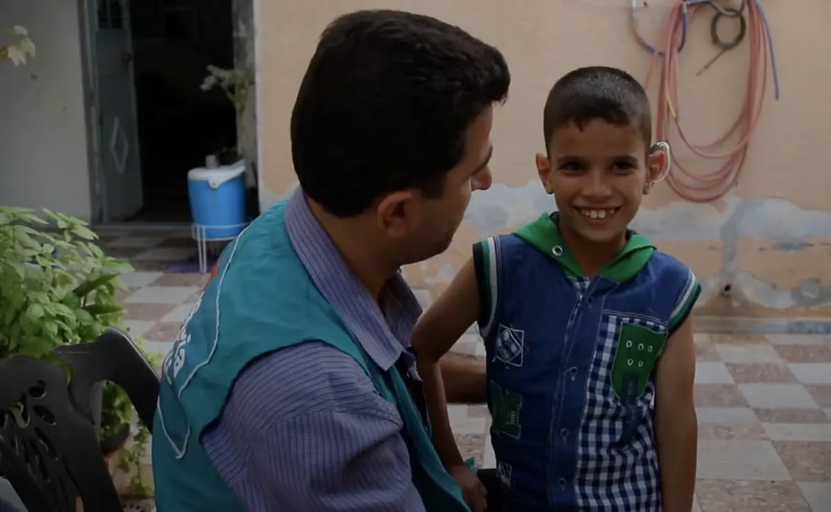 A doctor looks at a smiling child wearing a hearing aid device.
