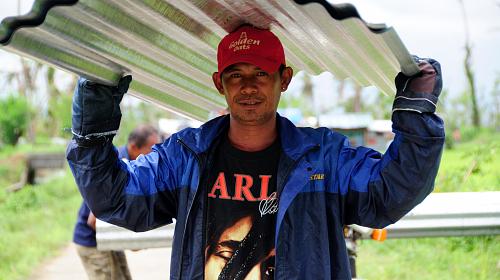A man carries corregated metal sheeting after receiving a shelter repair kit from CARE.