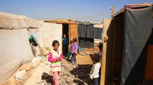 As crianças brincam fora de suas casas - compostas por barracas, madeira compensada e lonas - em um acampamento de refugiados em Zaatari, Jordânia.