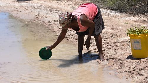 Women fetches water by the road as boreholes no longer function in Mozambique community. Credit: CARE