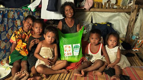 A CARE beneficiary and her grandchildren with their essential sack of CARE food items.Community members in typhoon-hit Patag village receive bags containing rice, sardines and canned meat from CARE and its local partner, ACCORD.