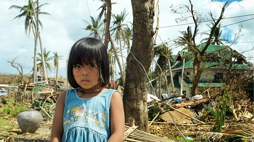 A young girl stands amongst the devastation after typhoon Haiyan hit her village in the Philippines. © 2013 Peter Caton/CARE