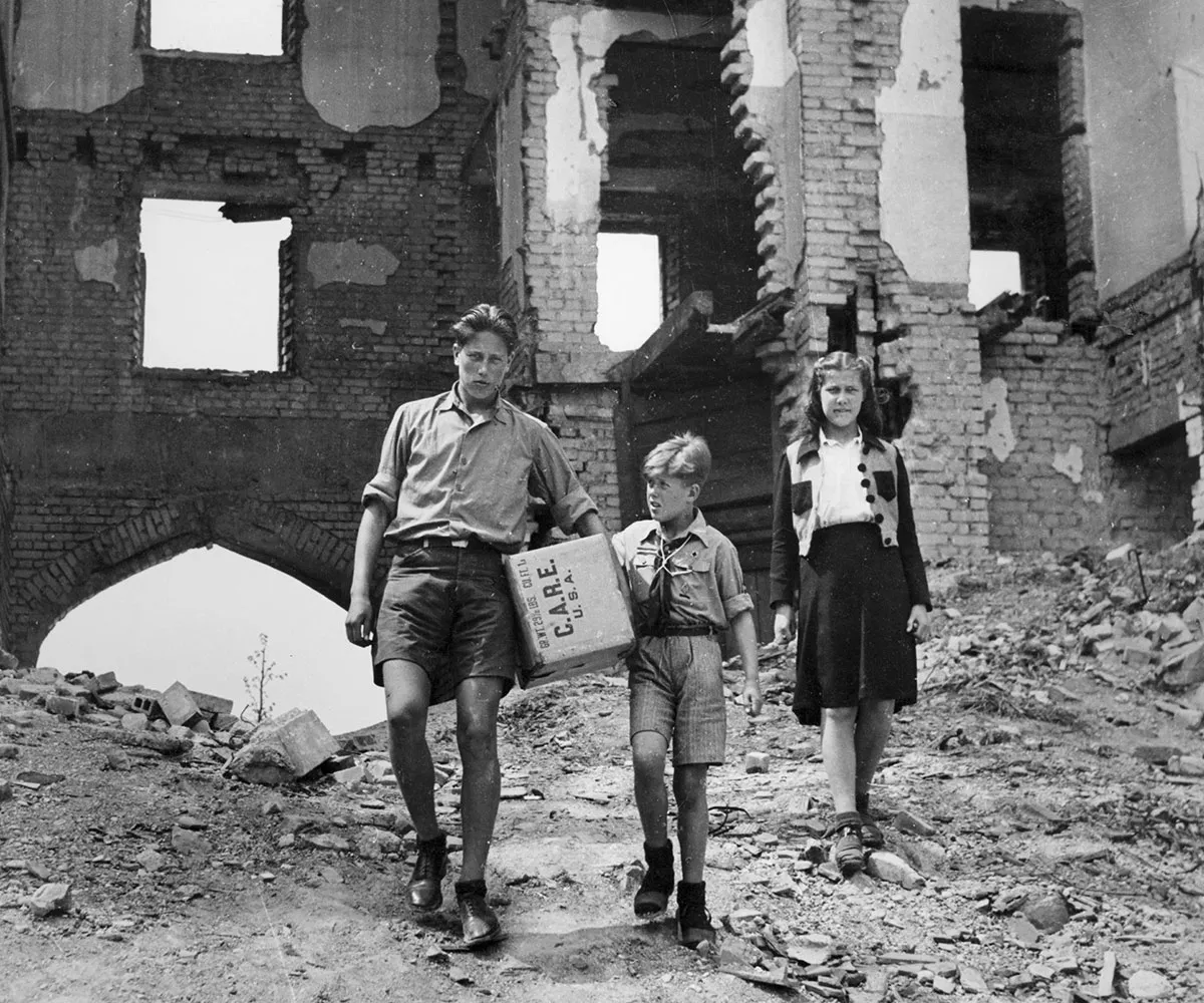 A man holding a CARE Package walks through the rubble of Berlin with his son and daughter.