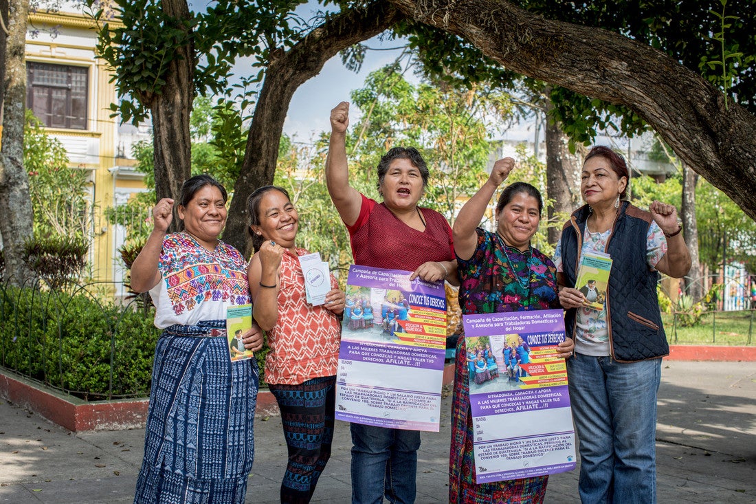 Um grupo de mulheres segura panfletos e comemora com as mãos levantadas.
