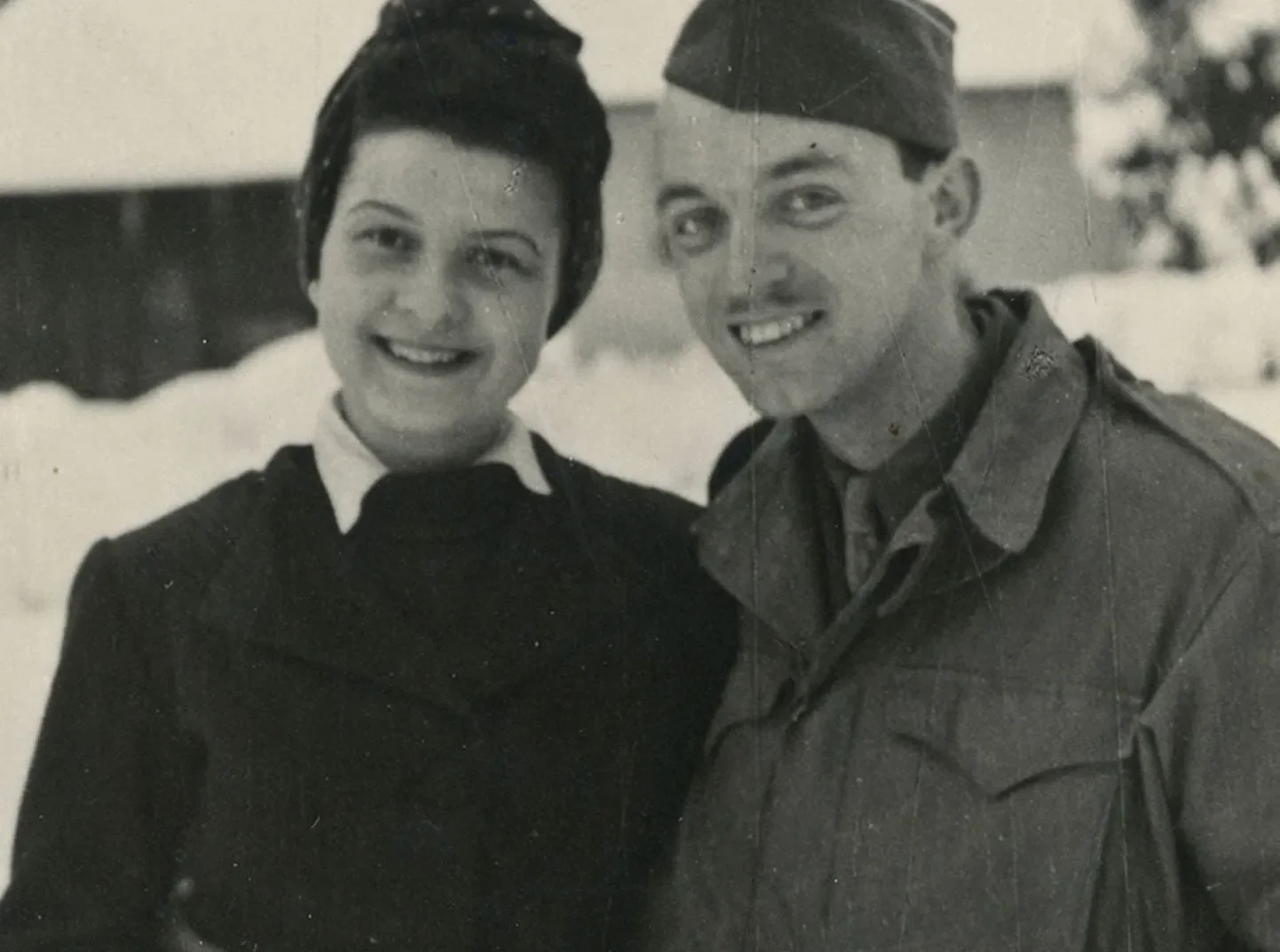 Uma velha imagem em preto e branco de um homem e uma mulher sorrindo e de pé na neve.