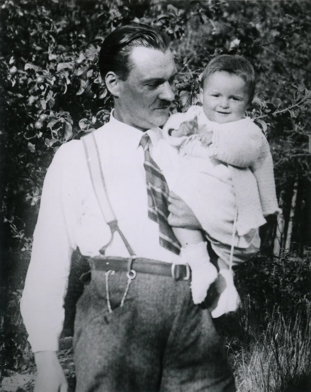 A man wearing a tie and suspenders holds a small girl.