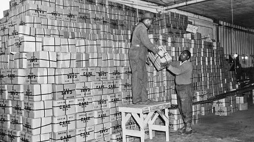Two men help prepare packages for shipment in a warehouse on Pier 38 on the Delaware River. CARE