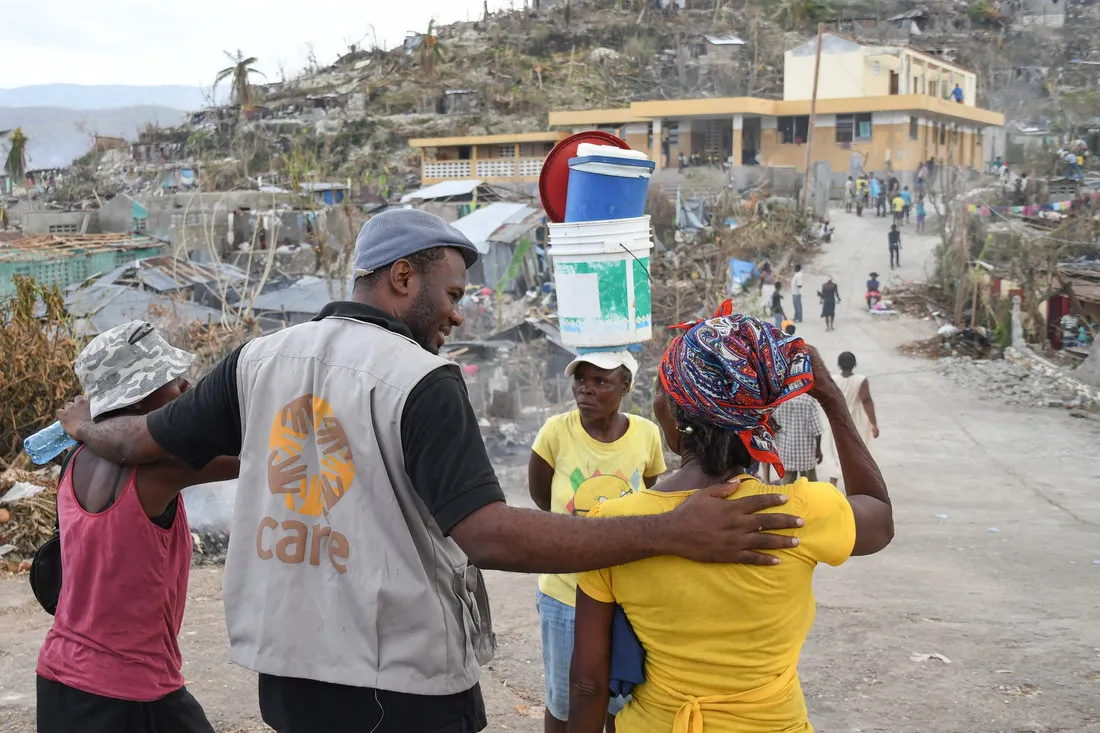 A male CARE staffer wearing a tan CARE vest walks with a small group of people down a road in Haiti.