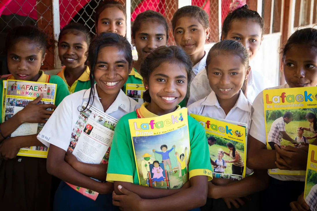 Un groupe de filles de l'école locale souriant et tenant des exemplaires de Lafaek Prima.
