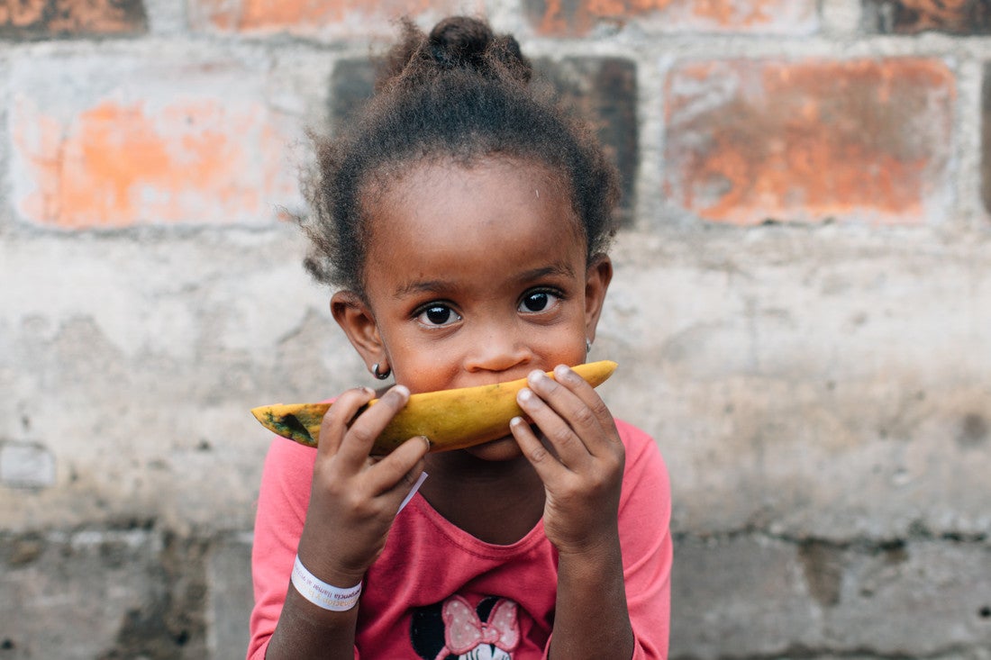 A young girl bites into a plaintain.