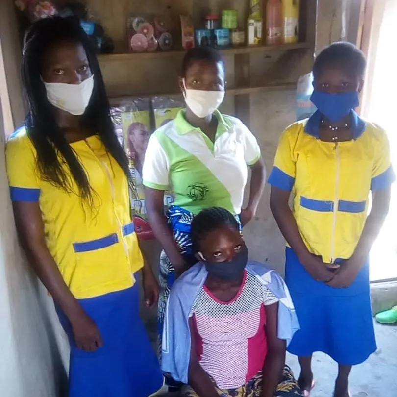 Un groupe de femmes au Bénin est assis à l'intérieur d'un bâtiment en bois sans porte tout en portant des masques pour aider à prévenir la propagation du coronavirus.