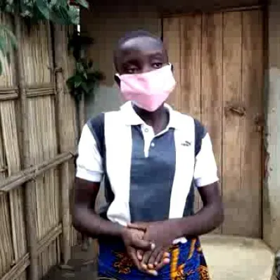Une femme porte un masque rose debout près d'une clôture en bois au Bénin.
