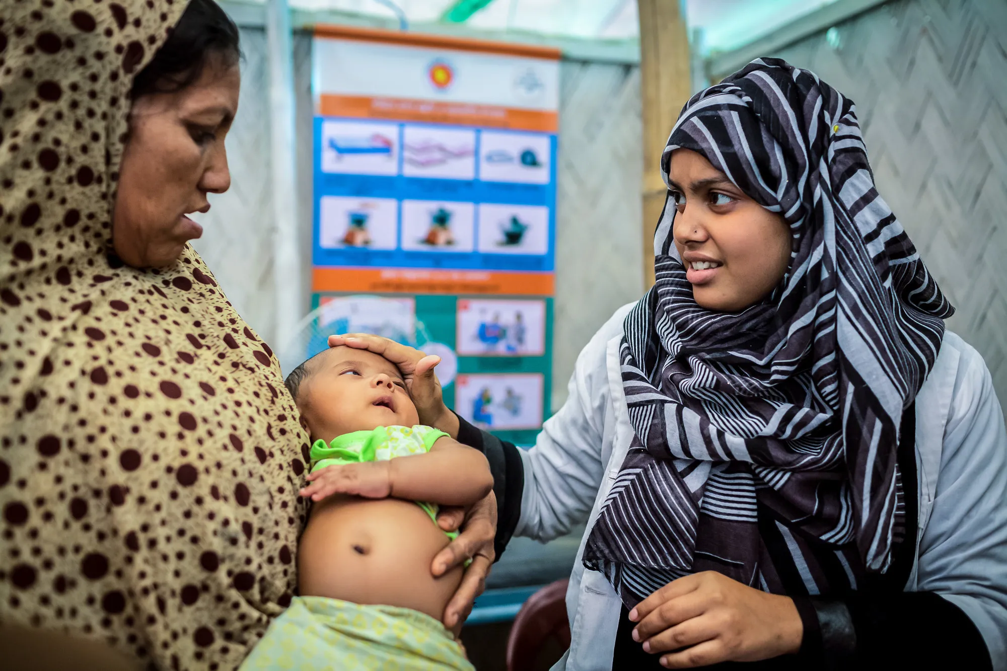 Une mère tient son bébé pendant qu'un agent de santé touche la tête du bébé dans une clinique au Bangladesh.
