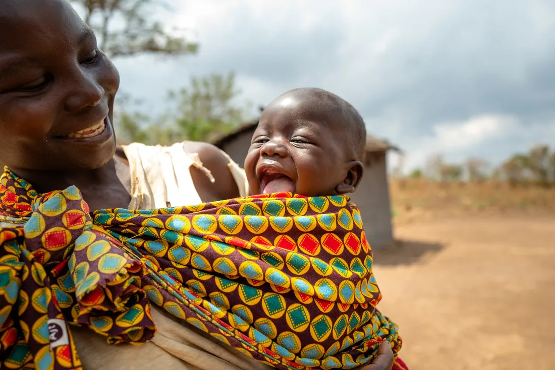 A woman smiles at her baby, who is smiling with his mouth wide open.