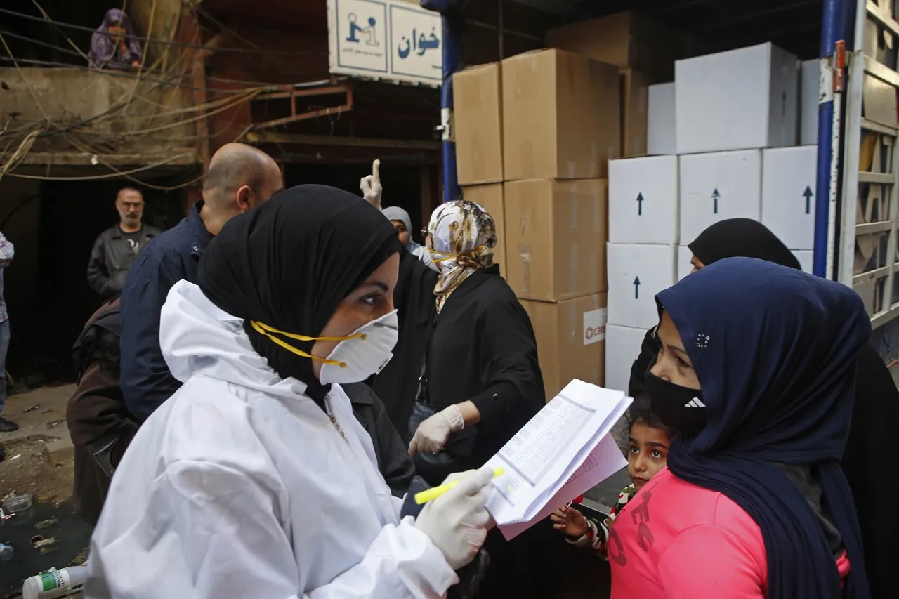 A equipe da CARE no Líbano, vestida com equipamentos de proteção e máscaras, distribui cestas básicas e itens de higiene na parte de trás de um caminhão de carga aberta.