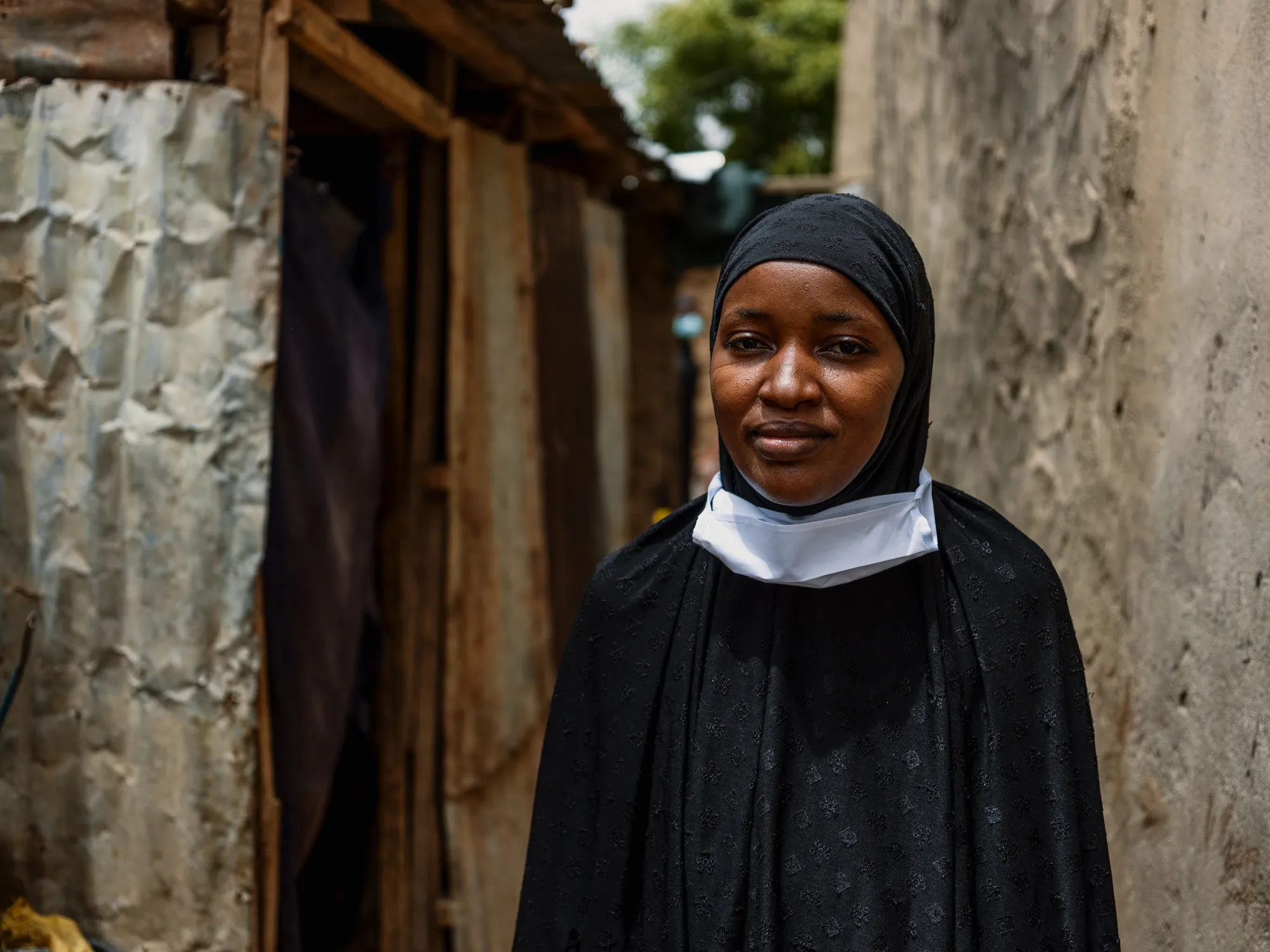 Una mujer de Níger se encuentra entre un muro de hormigón y una casa de madera y metal ondulado.