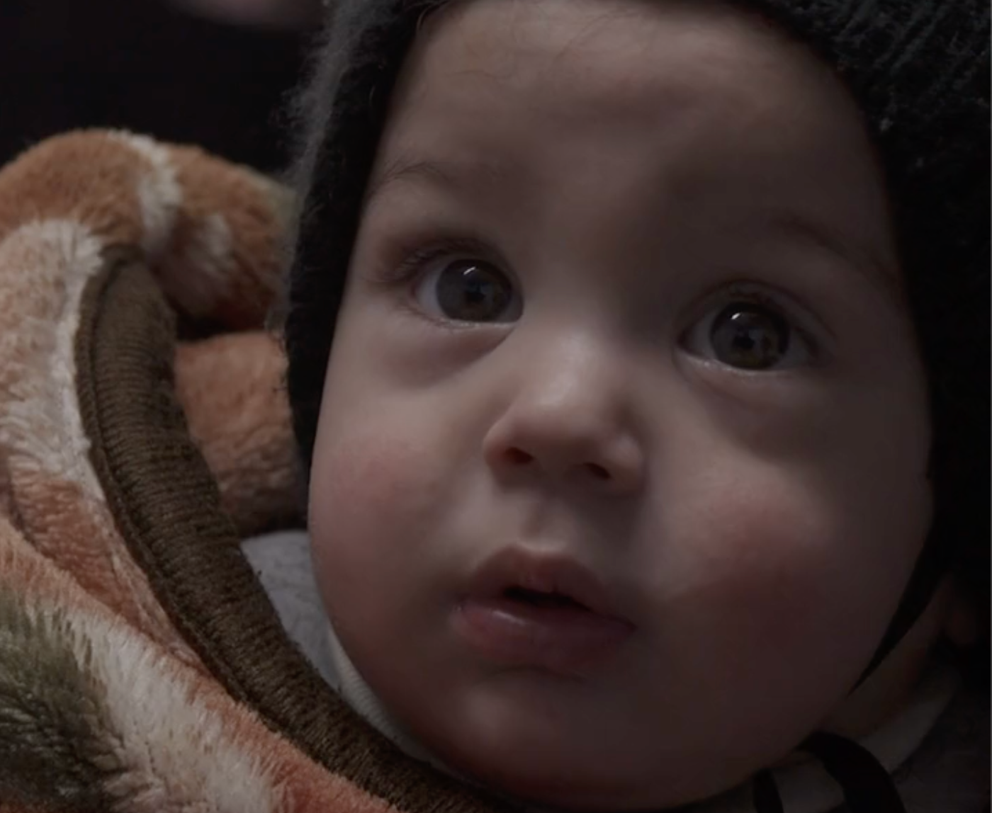 Um bebê sírio enrolado em cobertores e usando um chapéu.