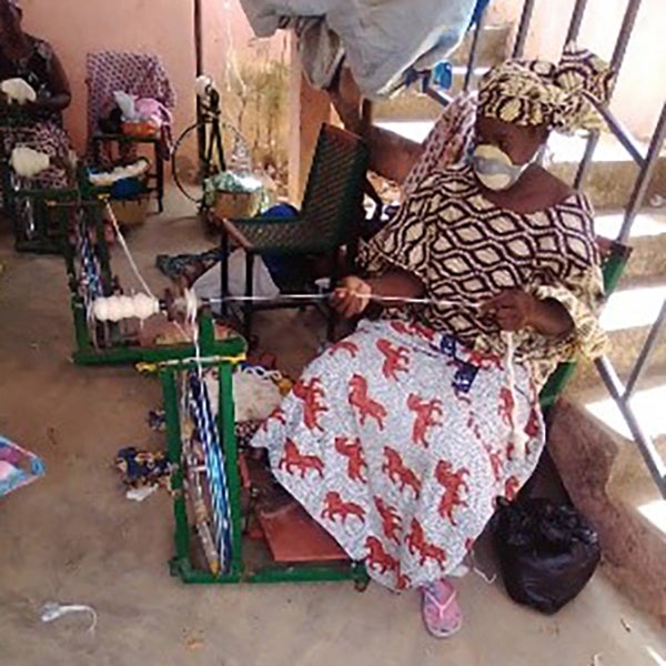A woman in a mask in Mali works in front of a loom.