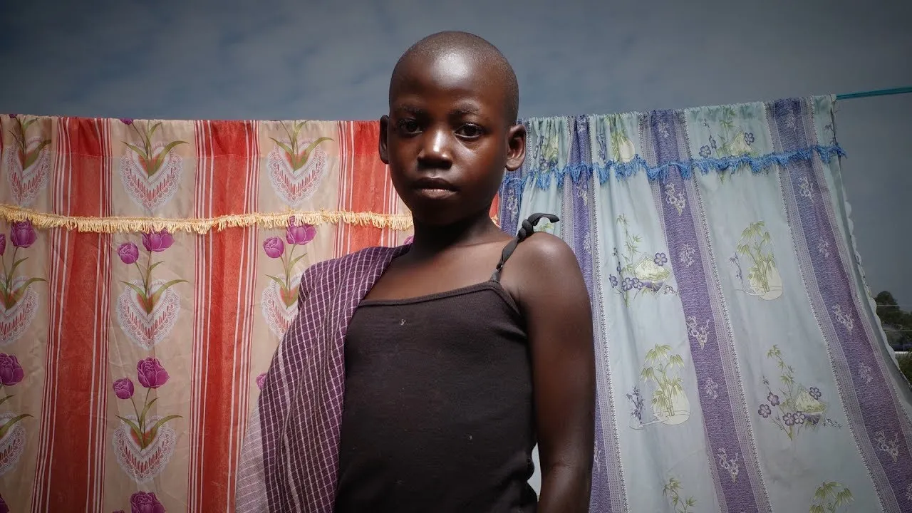 A young girl stands in front of two pieces of fabric hung on a string.
