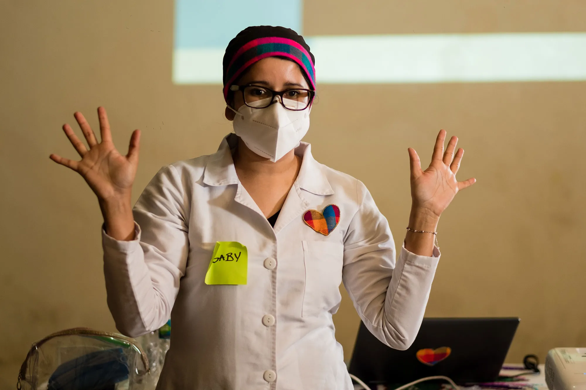 une femme en blouse de laboratoire et masque chirurgical parle avec ses mains en l'air.
