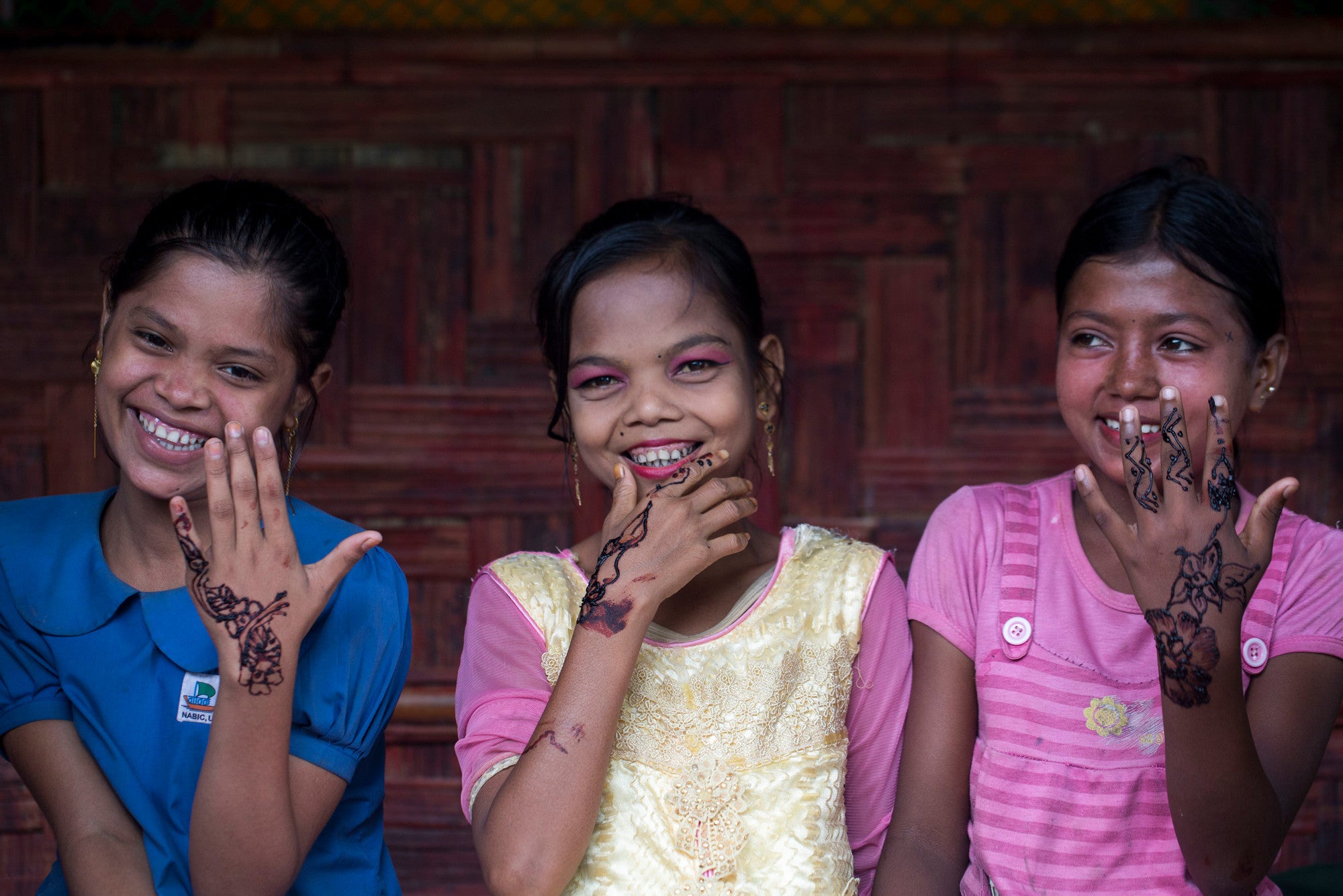 Three girls smile while displaying traditional decorations drawn on their hands.