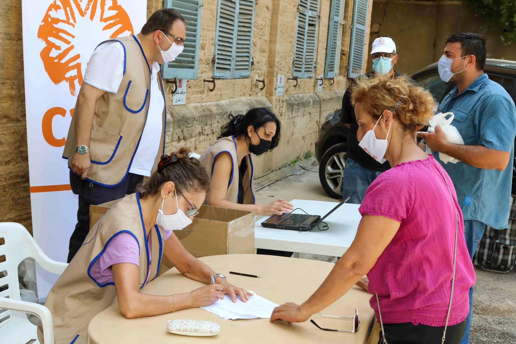 A woman worker in a mask fills out a form at a food distribution site in Beirut while another woman in a mask stands across the table from her.