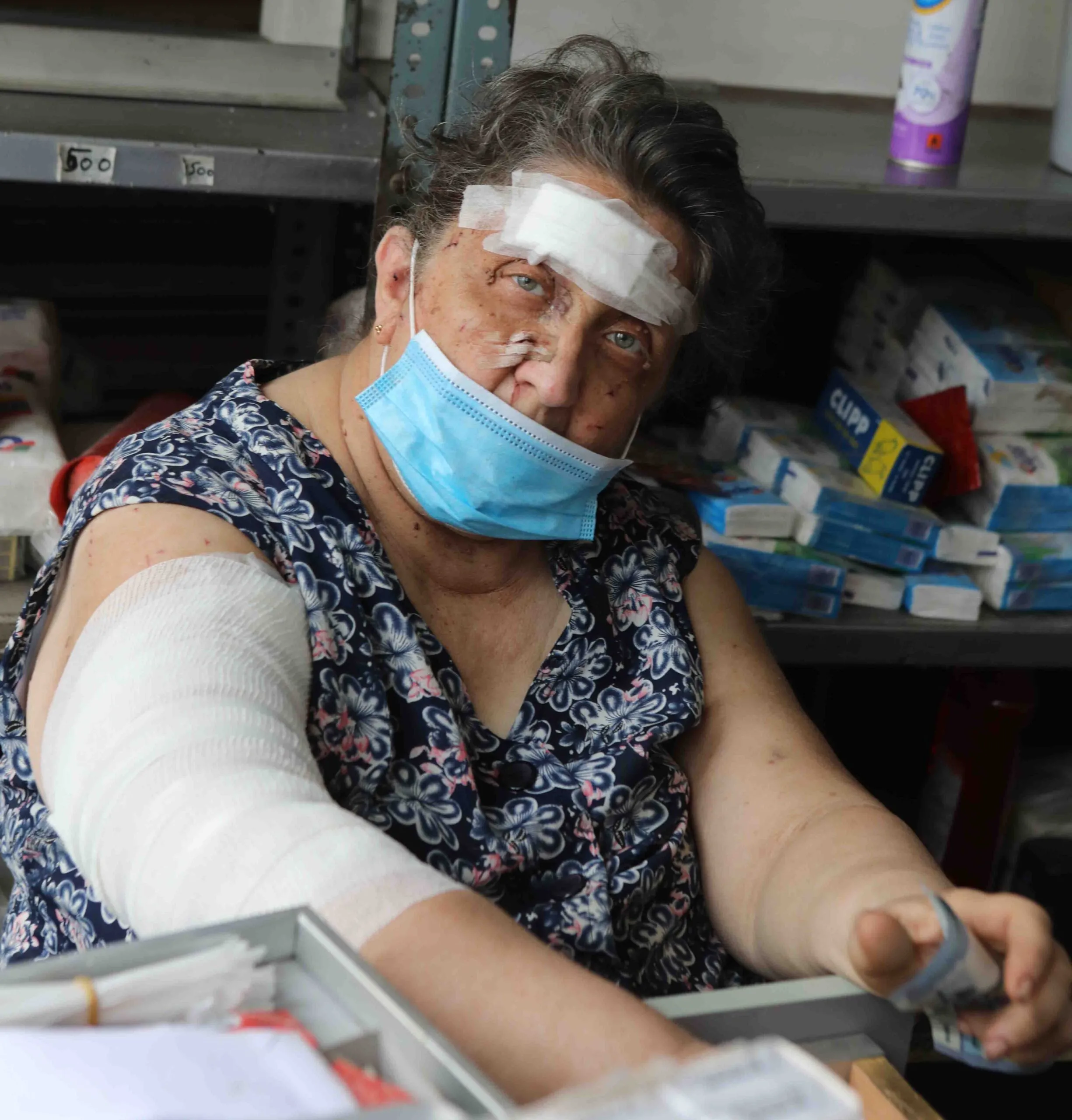 An elderly injured Lebanese woman with bandages on her head and right arm looks directly ahead.