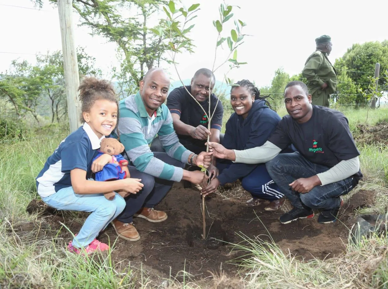 Un groupe de cinq adultes et enfants plante un petit arbre.