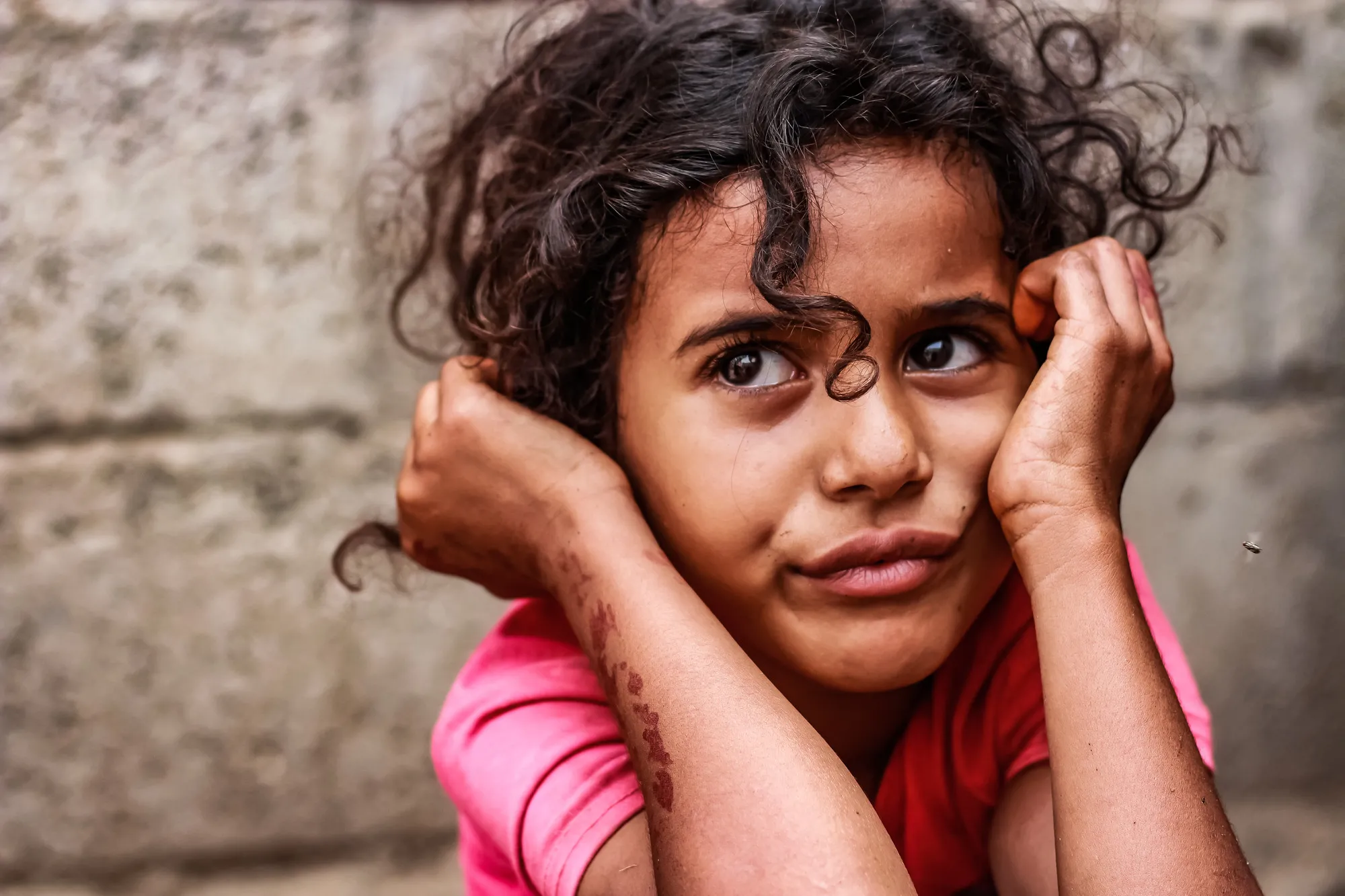 A young girl holds her head in her hands with a sad expression on her face.