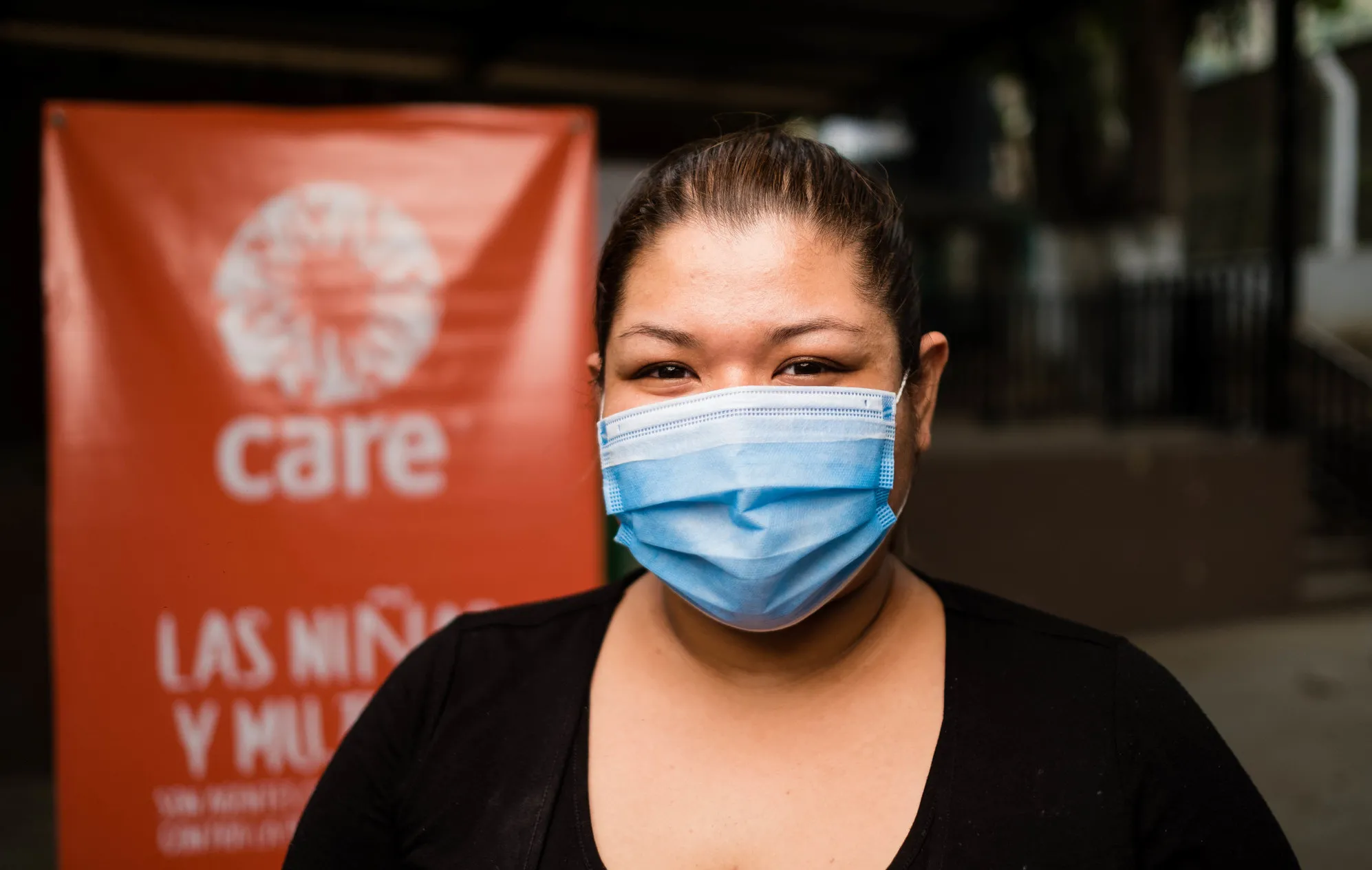 Une femme masquée se tient devant un panneau CARE.