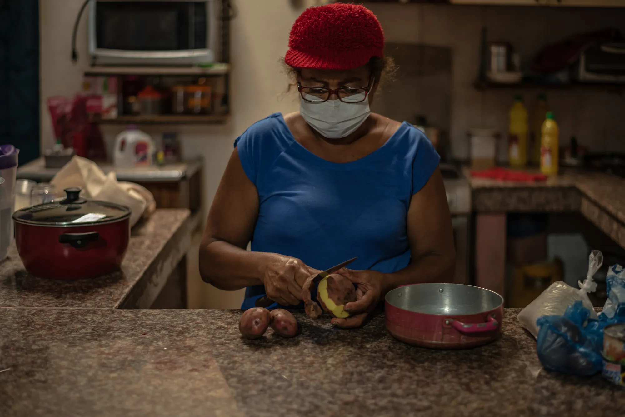 Uma mulher com uma máscara facial descasca uma batata na cozinha.