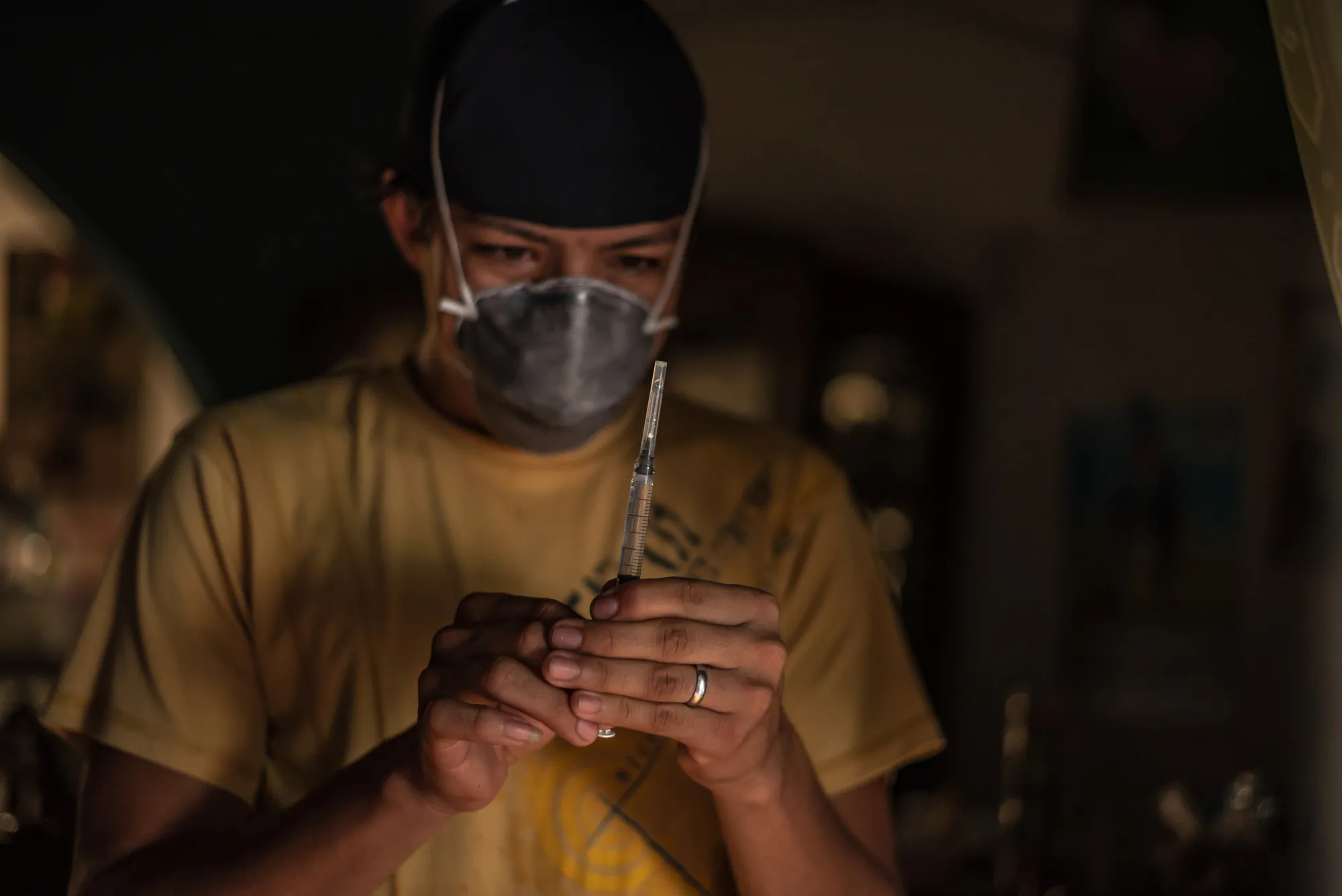 A man in a face mask looks at a syringe
