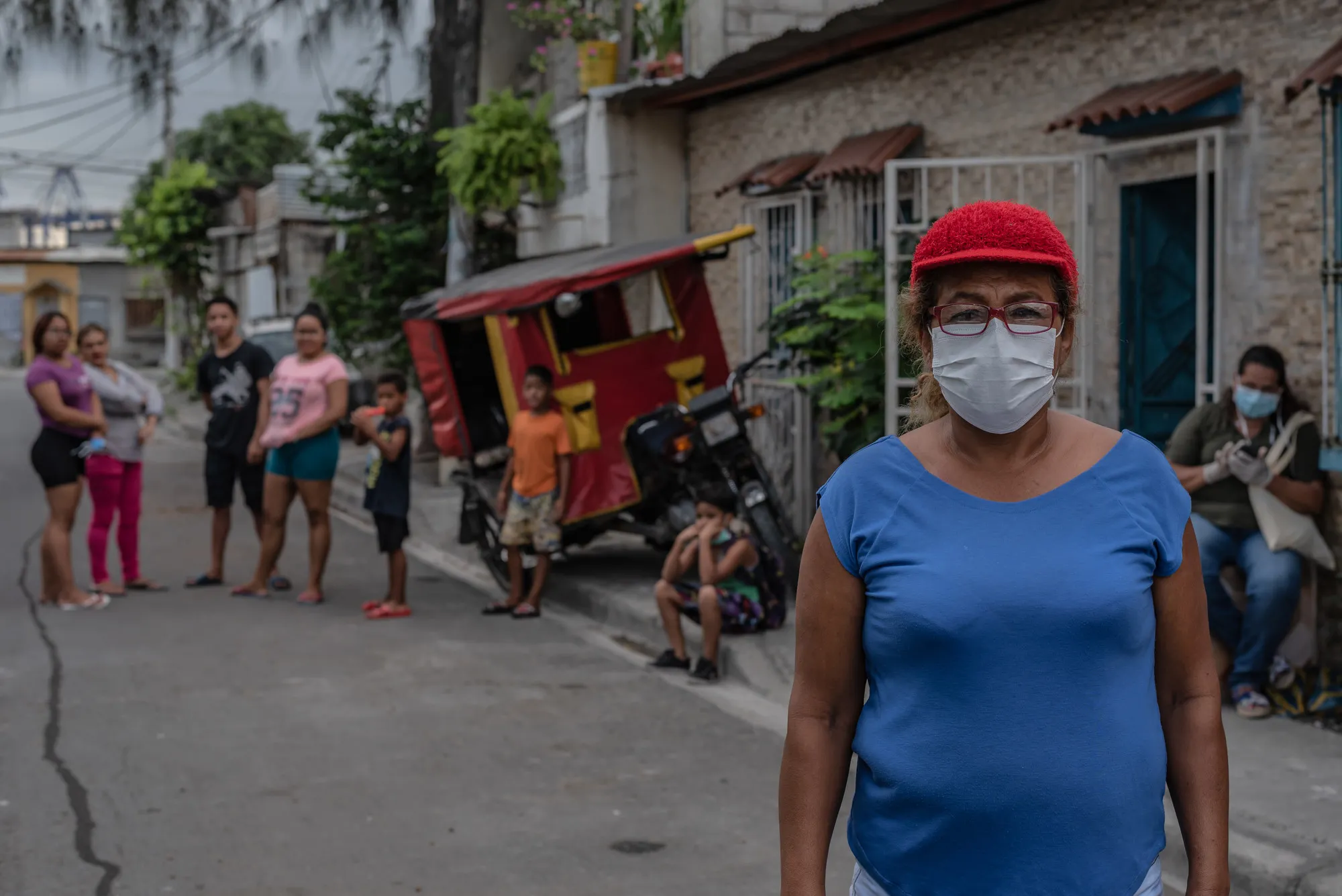 A woman in a hat and face mask stands in a city street in front of her apartment