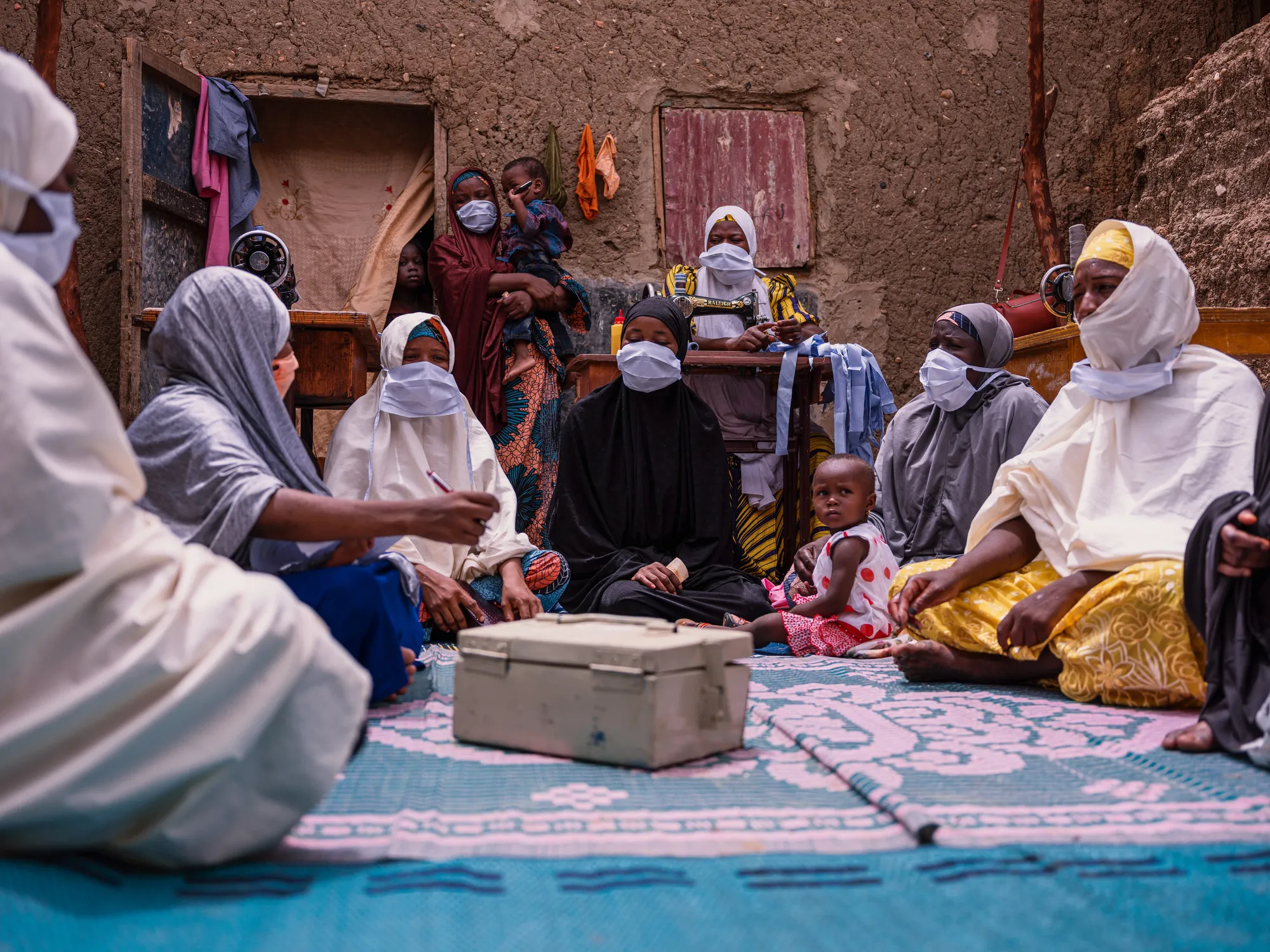 Un grupo de mujeres en una reunión mientras están sentadas en una alfombra con una caja de dinero.