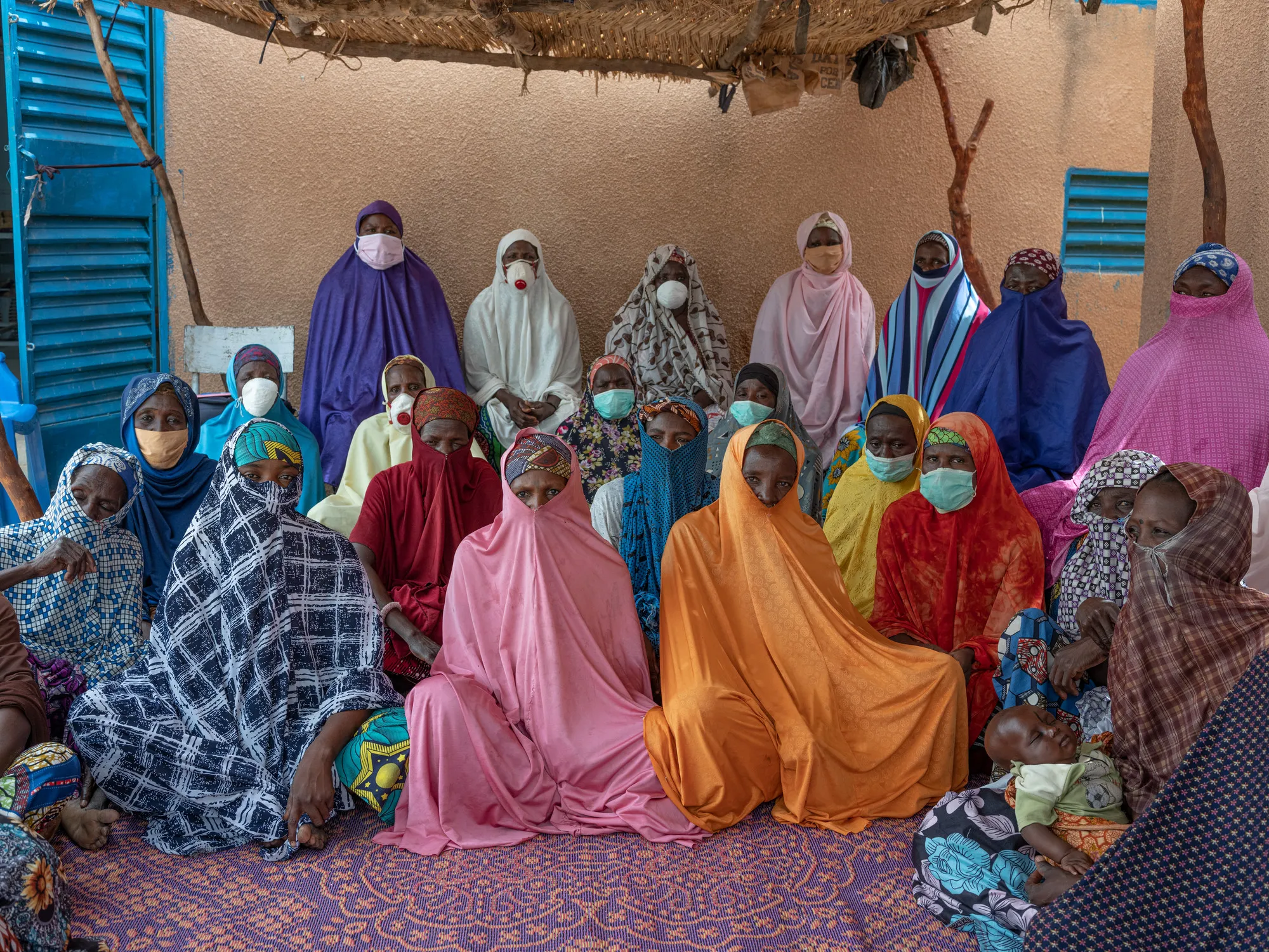 A group of women in colorful robes and face masks pose in rows facing forward.