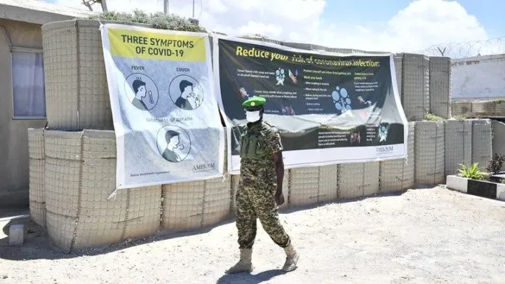 Un soldat passe devant une banderole COVID-19 au quartier général du secteur XNUMX à Mogadiscio, en Somalie. Photo par: AMISOM Photo / Steven Candia