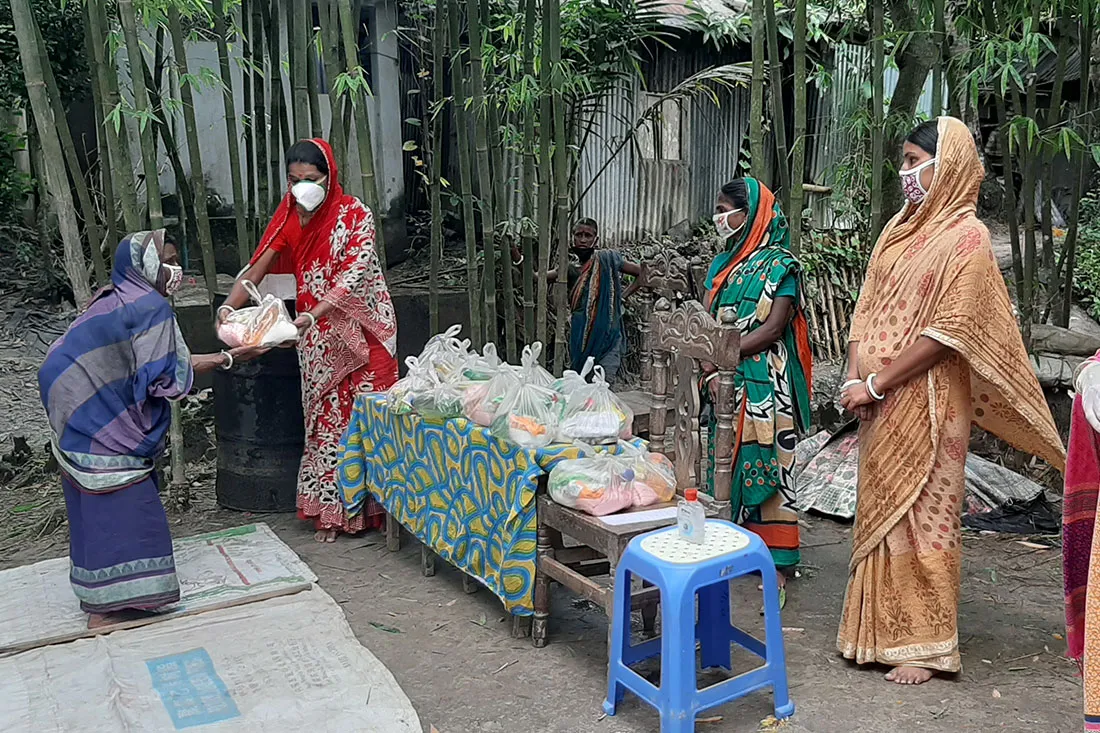 A group of women wearing brightly colored clothing and white face masks sort through supplies.