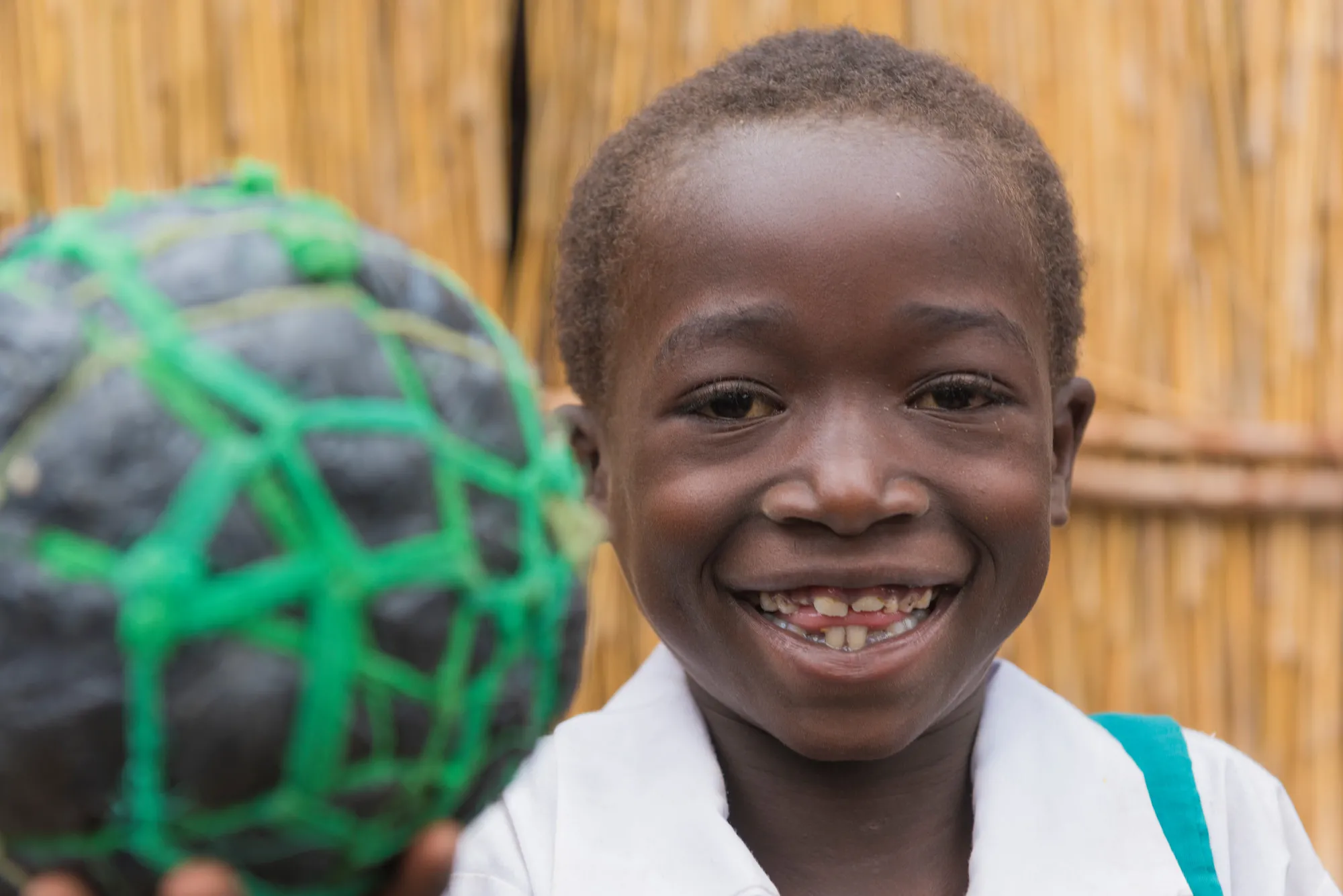 A young girl smiles wile holding an improvised soccer ball made of string and plastic bags.
