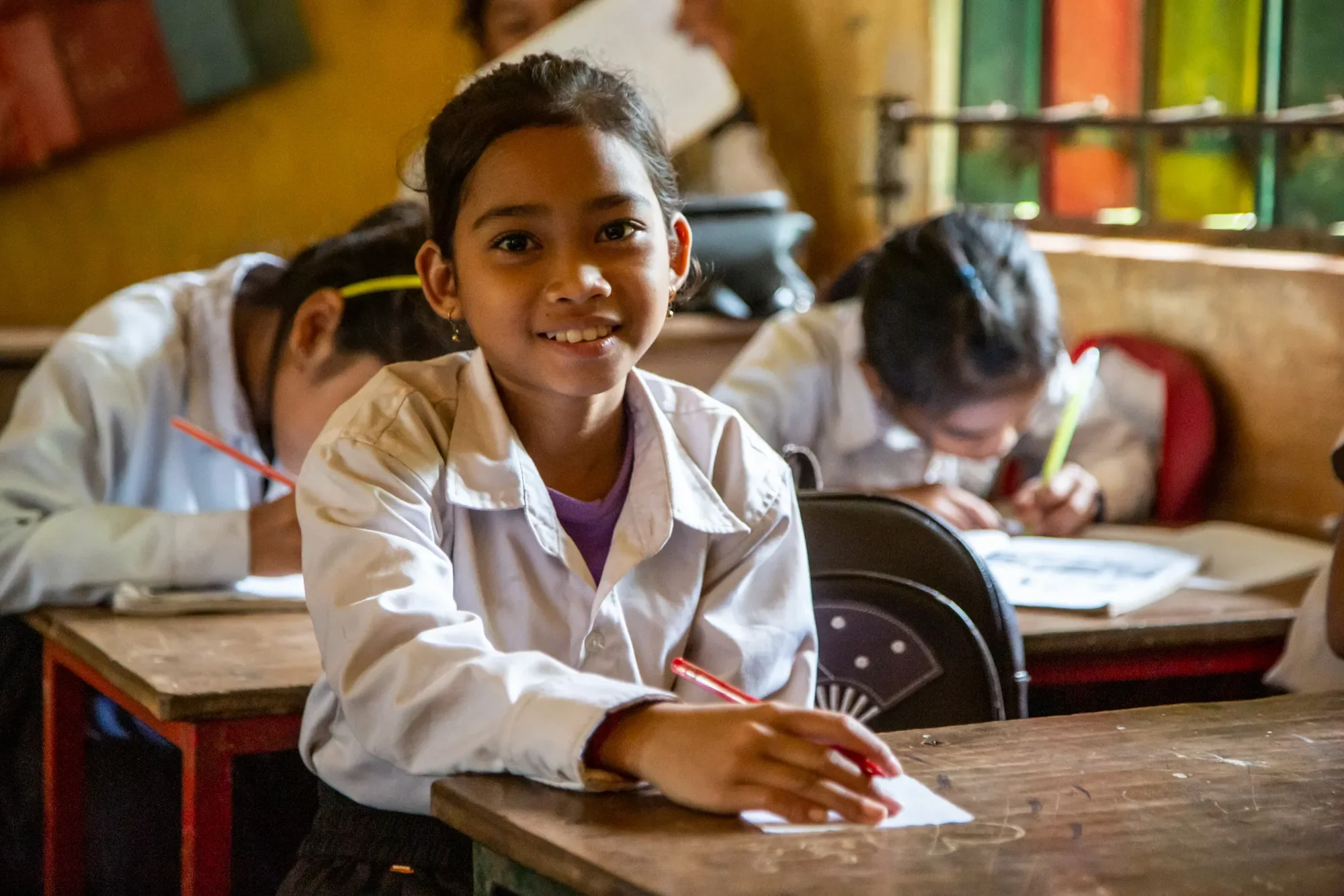 A girl sitting in a classroom smiles.
