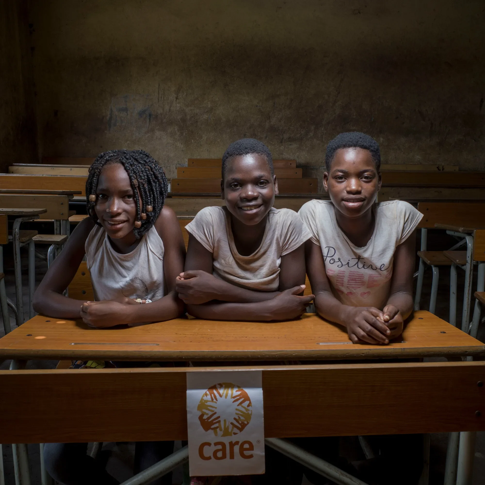 Trois adolescentes sont assises à un bureau en bois dans une salle de classe.