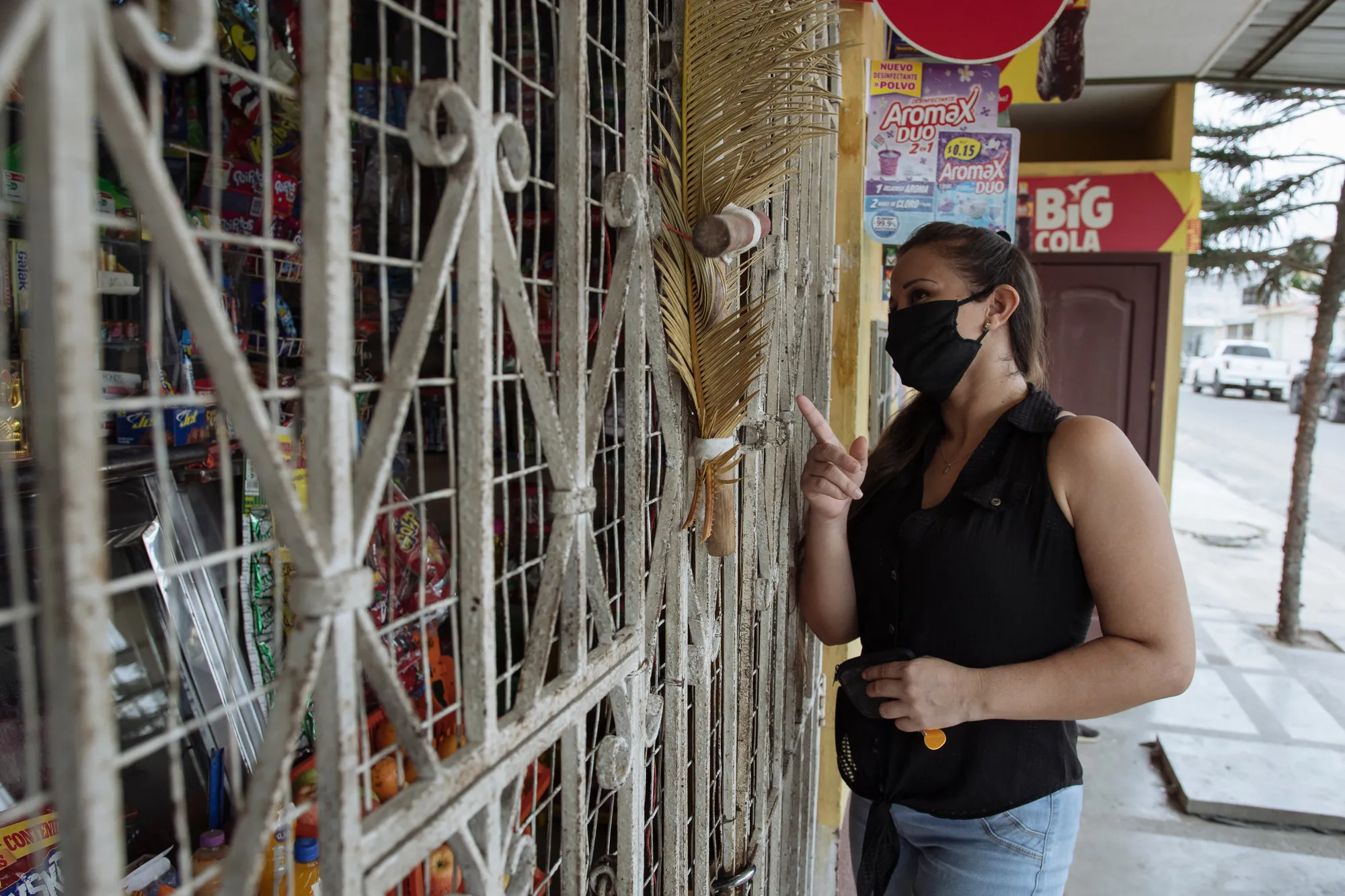A woman in a face mask stands outside of a small store in a city.