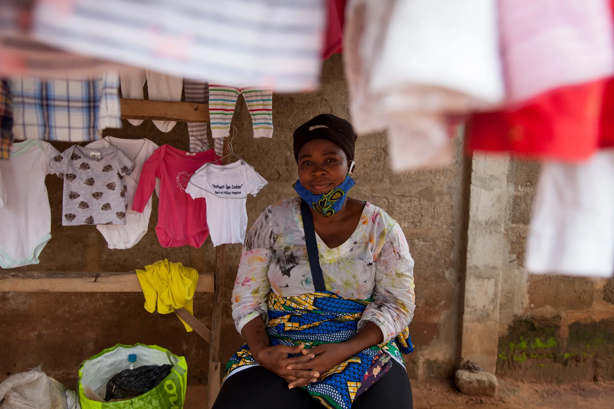 A woman sits in a stall selling clothes in an open-air market.