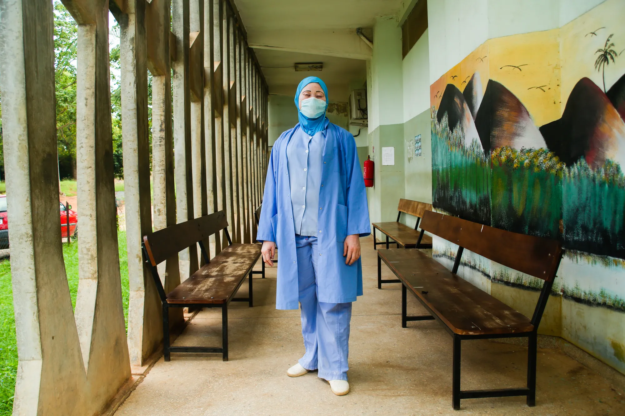 A woman in face mask and scrubs stands in a hallway.