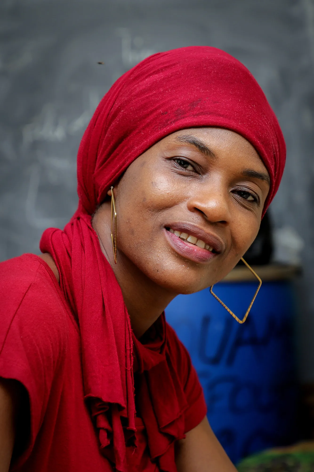 A woman in a red head wrap sits and smiles.