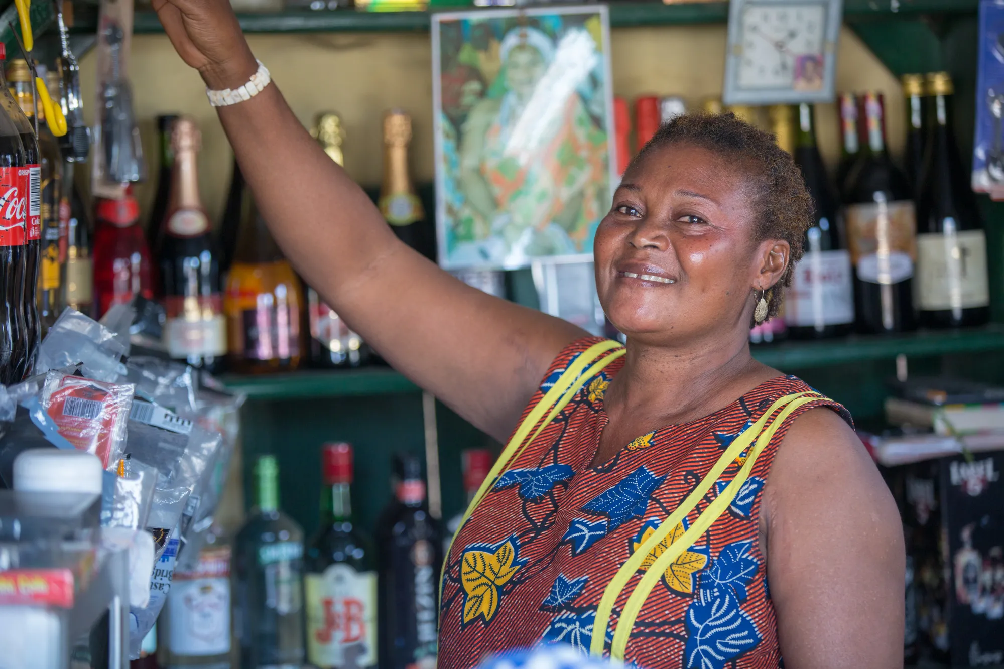 A woman smiles while reaching up to a shelf in a bar.