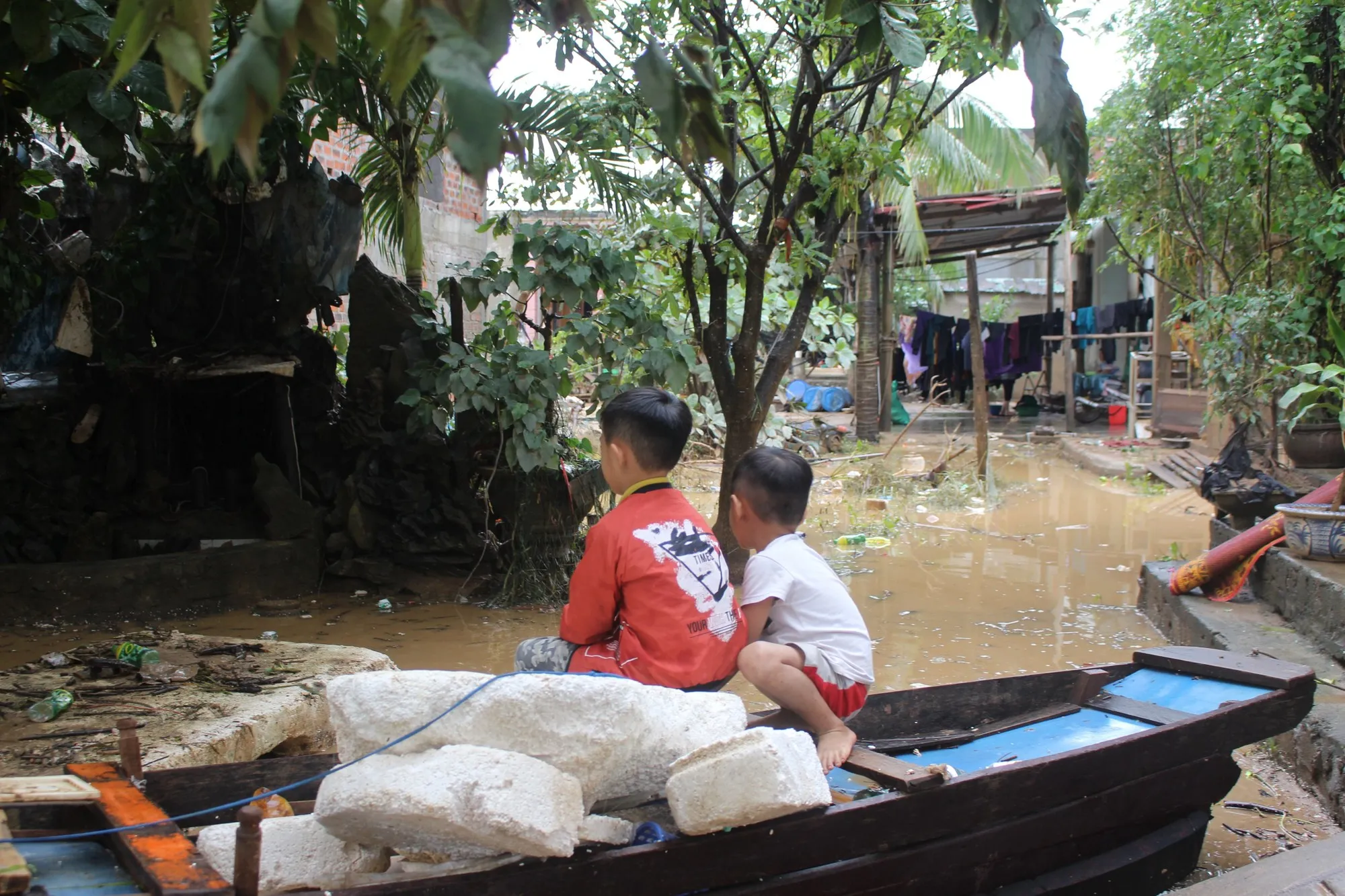 two children sit on a small boat in a flooded village.