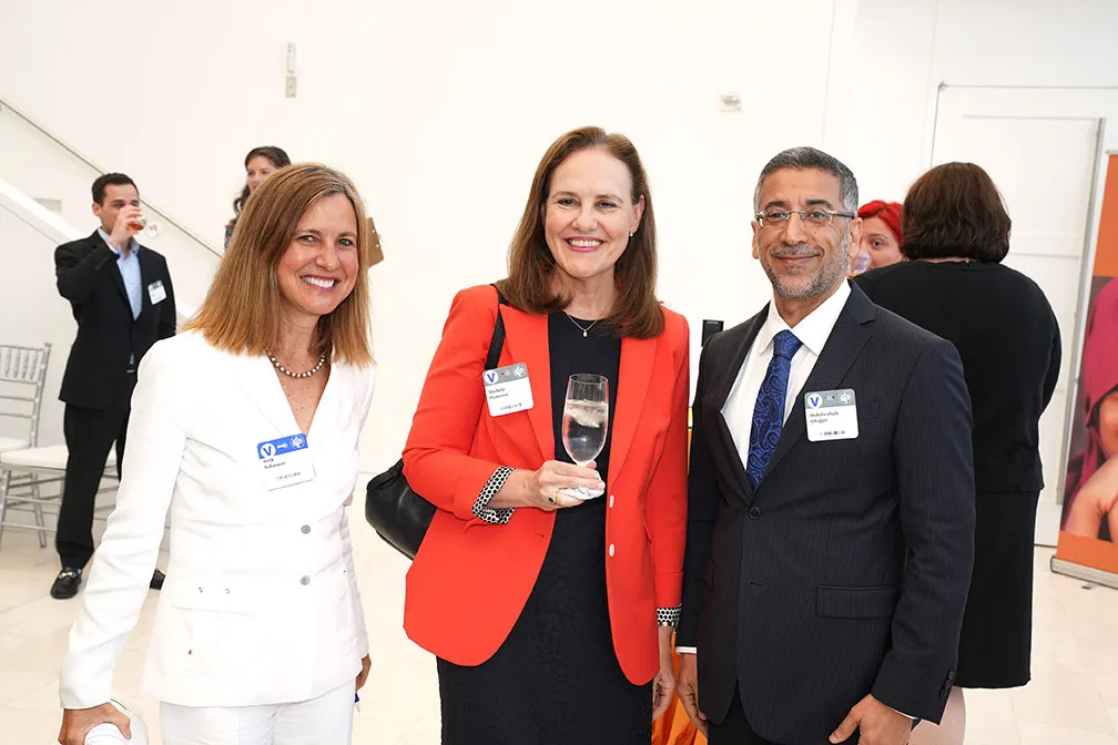 Michele Flournoy, former U.S. Undersecretary of Defense for Policy, wears a red blazer. She is posing for the camera with a woman wearing all-white and a man wearing a suit.
