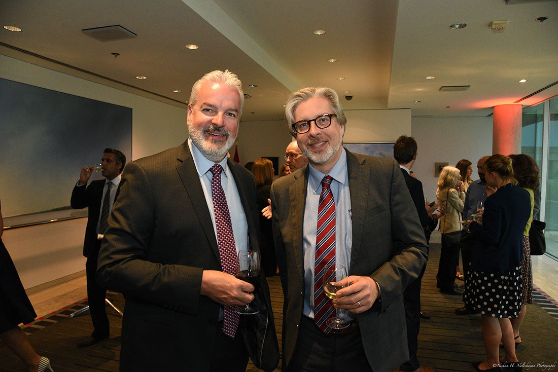 Two attendees of the event, both wearing suits and ties, smile for the camera while enjoying wine.