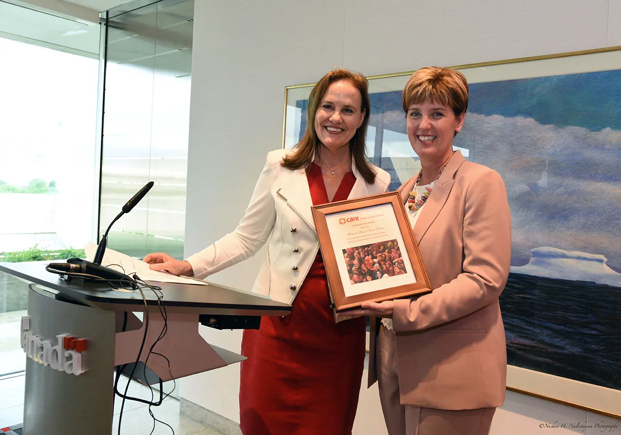 Former Under Secretary of Defense Michéle Flournoy, wearing a red dress and white jacket, stands with Minister Marie-Claude Bibeau, wearing a blush pink suit, as Minister Bibeau accepts a CARE Global Leaders Network Humanitarian Award.