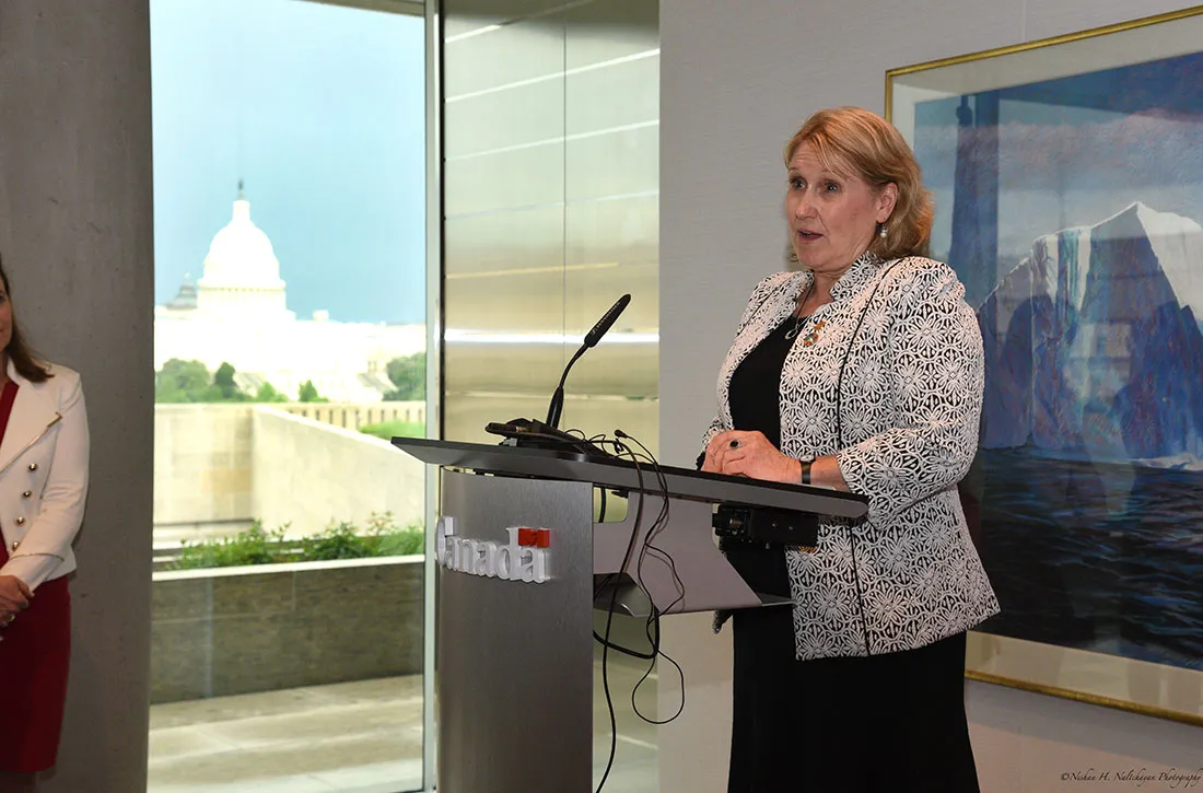 A woman wearing a black and white patterned jacket speaks at the podium at the Embassy of Canada.